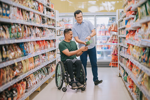 asian indian man with disability on wheelchair shopping at supermarket during weekend with friend