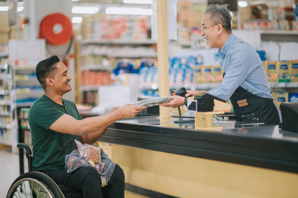 asian indian man with disability on wheelchair check out at cashier supermarket during weekend asian indian man with disability on wheelchair check out at cashier supermarket during weekend accessibility for persons with disabilities photos stock pictures, royalty-free photos & images