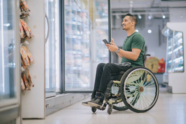 asian indian man with disability on wheelchair shopping at refrigerated section supermarket for frozen food during weekend asian indian man with disability on wheelchair shopping at refrigerated section supermarket for frozen food during weekend refrigerated section supermarket photos stock pictures, royalty-free photos & images