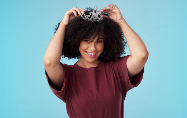 studio strzał młodej kobiety oddanie korony głowę na niebieskim tle - women crown tiara princess zdjęcia i obrazy z banku zdjęć