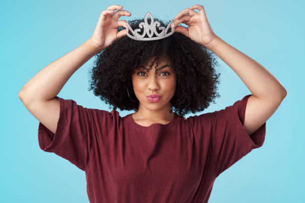 Studio shot of a young woman putting a crown her head against a blue background Fix your crown, never let it fall beauty queen stock pictures, royalty-free photos & images