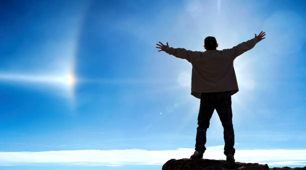 istock Cheering man open arms on mountain peak cliff over blue sky background 1321243446