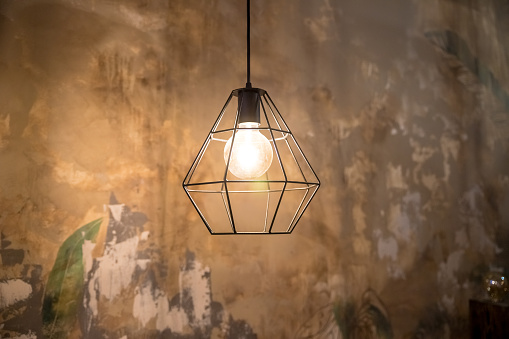 Industrial style wire lamps with filaments glowing inside glass light bulbs in darkness. Shiny lights and dark background. Urban style interior lighting with cage lampshades. Grunge decoration.