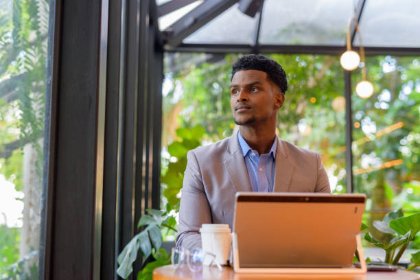 istock African businessman at coffee shop using laptop computer and thinking while looking through window 1321246766