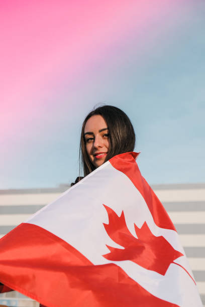 young millennial brunette woman holding the national flag of canada. canadian flag or the maple leaf. tourist traveler or patriotism. immigrant in a free country. independence day 1th july - canadian flag fotos imagens e fotografias de stock