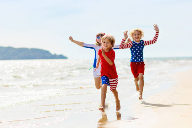 Kids with American flag on beach. 4th of July. Kids run with USA flag on sunny beach. 4th of July celebration. American family fun on Independence Day weekend. Patriotic children celebrate US holiday. Boy and girl with symbols of America. family beach vacations travel stock pictures, royalty-free photos & images