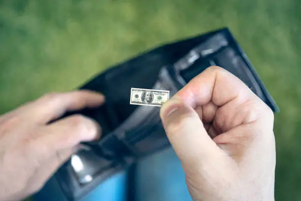 Photo of A male businessman opens a black wallet and pulls out a hundred-dollar bill on a green background. a small salary for an employee. concept of dollar inflation. Hand holding miniature dollar note