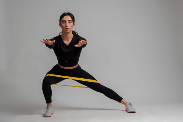istock Girl doing side lunges with resistance band on grey background 1321252927