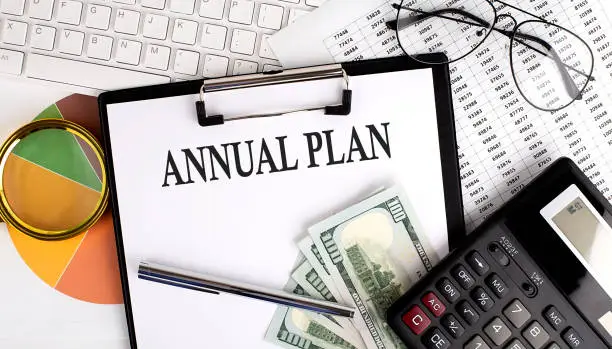 Photo of Text ANNUAL PLAN on Office desk table with keyboard,dollars,calculator ,supplies,analysis chart on white background.