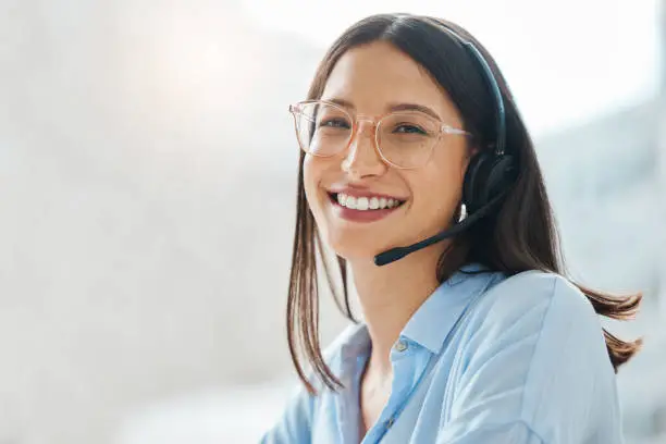 Photo of Shot of an attractive young saleswoman sitting alone in the office and wearing a headset