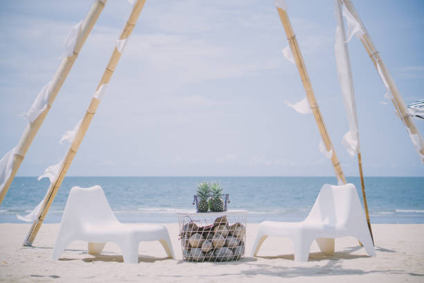 istock Two white chairs and a table on the sandy beach against the sea backdrop. 1321257378