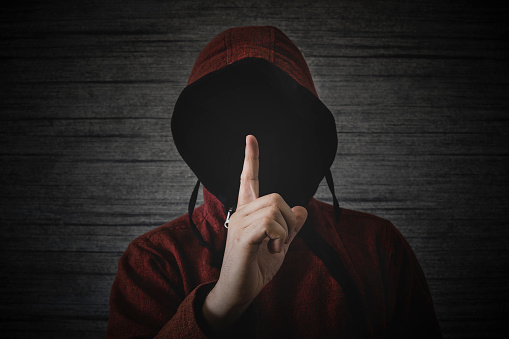 an unknown person without a face in a hood shows a finger gesture meaning towns. The concept of anonymity and secrecy in the network.
