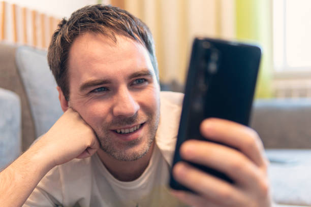 istock A young guy is resting on the couch and reading information from a smartphone. Online video chat. Happy male using smartphone at home, he chatting Online Messaging on mobile. 1321258584