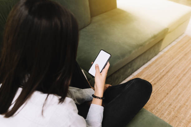 istock Girl sitting on green sofa and holding smartphone with empty white screen 1321260375