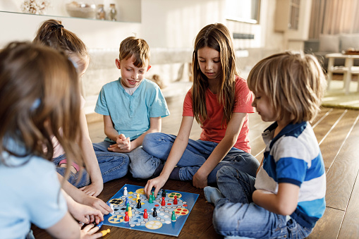 Group of small friends playing ludo game on wooden floor at home.