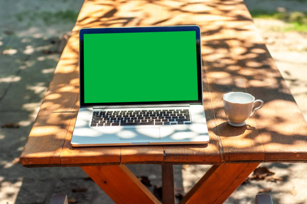 istock View on a laptop pc with a green screen and a coffee mug on a table in the garden 1321265715
