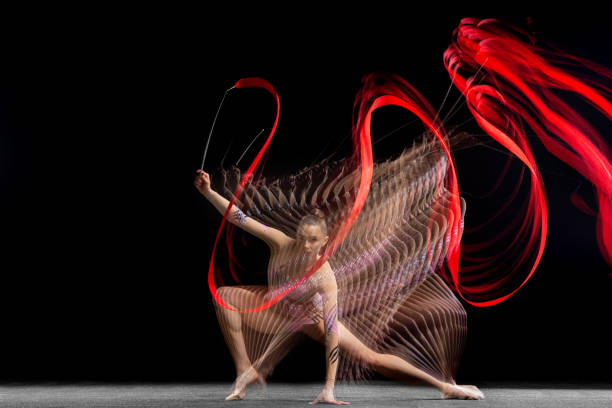 joven chica grácil gimnasta rítmica en movimiento aislado en luz mixta sobre fondo oscuro. - stroboscopic image fotografías e imágenes de stock