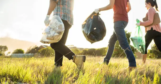 Diverse group of young volunteers walking together through a field during a community litter cleanup day