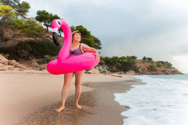 Photo of Happy senior woman on the beach with inflatable flamingo ring