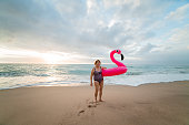 Happy senior woman on the beach with inflatable flamingo. Active senior concept.