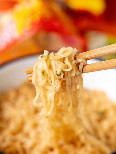 Hot, ready to eat, Asian instant noodles on chopsticks. The most popular Asian fast food, available internationally, here a mouthful of freshly heated instant noodles are on chopsticks, ready to be eaten. Shallow depth of field with the focus being on the noodles at the end of the bamboo disposable chopsticks. Good copy space above the image. cooked selective focus vertical pasta stock pictures, royalty-free photos & images