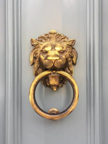 Gold lion head door knocker with the ring on its mouth on the entrance of a house, Malta. Italian traditional doorknob. Old ornate metal door handle.