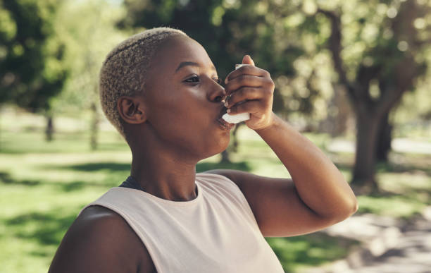 colpo di una giovane donna che si prende una pausa durante un allenamento per usare la pompa per l'asma - asthmatic foto e immagini stock