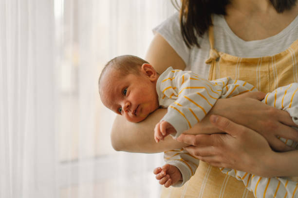 Mother playing with newborn baby son at home near the window. Happy infant and mom. Mother playing with newborn baby son at home near the window. Happy infant and mom. Isolation during quarantine on Mother's day cute boy show love symbol hand stock pictures, royalty-free photos & images