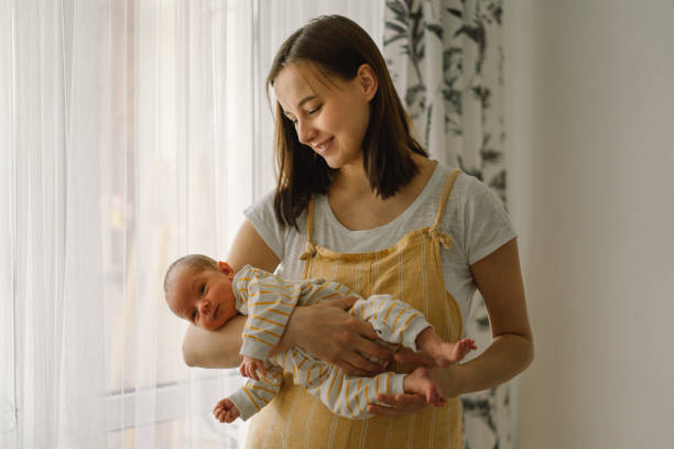 Mother playing with newborn baby son at home near the window. Happy infant and mom. Mother playing with newborn baby son at home near the window. Happy infant and mom. Isolation during quarantine on Mother's day cute boy show love symbol hand stock pictures, royalty-free photos & images