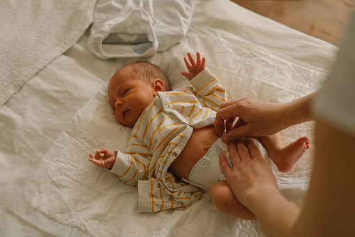 Mom changing his diaper newborn baby. Happy young mother playing with baby while changing his diaper on bed. Happy motherhood. Infant baby. Mother's day