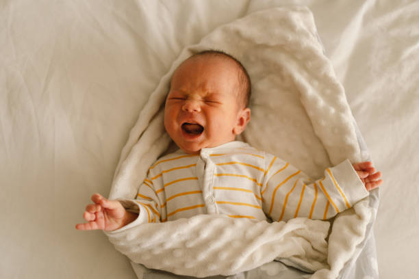 Cute emotional newborn little baby boy cry in crib. Tummy hurts and  emotion Cute emotional newborn little baby boy cry in crib. Tummy hurts and  emotion. Infant baby. baby sleeping bedding bed stock pictures, royalty-free photos & images