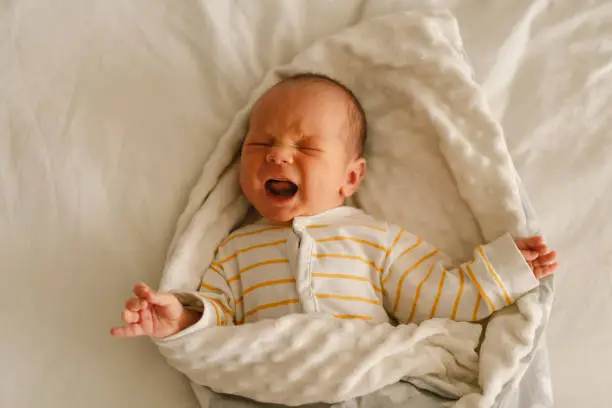 Cute emotional newborn little baby boy cry in crib. Tummy hurts and  emotion. Infant baby.