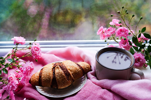 sweet fresh morning coffee and croissant staying on the windowsill with pink flowers