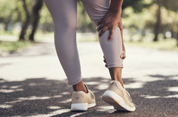 shot of a woman massaging an injury in her leg - leg imagens e fotografias de stock