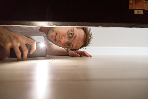 Hombre con linterna mirando debajo de la cama photo