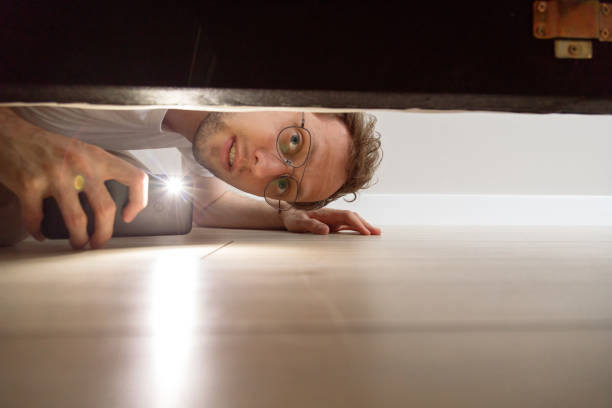 hombre con linterna mirando debajo de la cama - debajo de fotografías e imágenes de stock