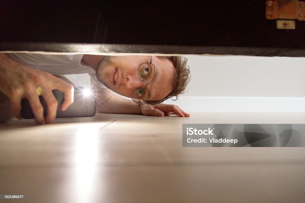 Man with flashlight looking under the bed Man with flashlight looking under the bed. Searching Stock Photo