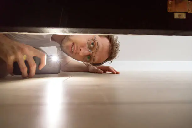 Photo of Man with flashlight looking under the bed