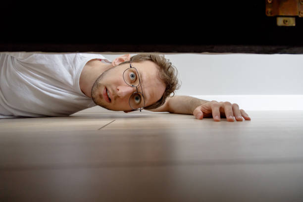 hombre con sorprendentemente mirando debajo de la cama - looking at view flash fotografías e imágenes de stock