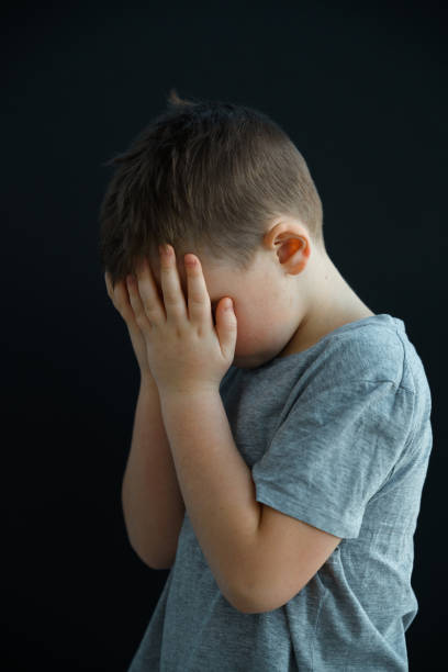 un niño pequeño está llorando, se cubrió la cara con las manos, tal vez alguien lo ofendió o sus padres lo castigaron. - displeased child abandoned child abuse fotografías e imágenes de stock