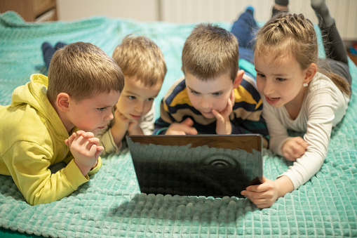 Group of preschool children smiling and playing video games on laptop at home.