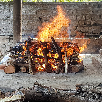 A pyre with burning wood and flames in outdoors during daytime in a Hindu crematorium in Bangalore. India witnessing mass cremation of those who died from the coronavirus disease COVID-19 second wave.
