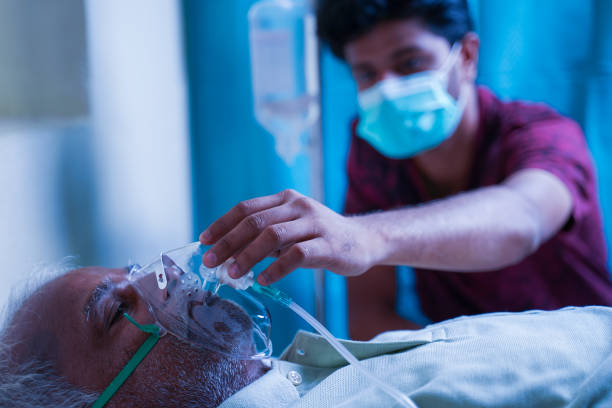 hijo con máscara facial médica que cuida del viejo padre enfermo en el hospital mediante la comprobación de la máscara de oxígeno ventilador - concepto de personas mayores atención médica parental y médica. - ventilador equipo respiratorio fotografías e imágenes de stock