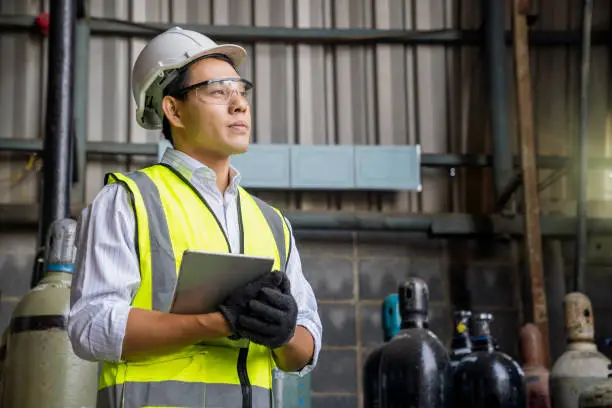 Industrial worker holding tablet in manufacturing gas. Acetylene and oxygen gas steel storage tanks for factory.