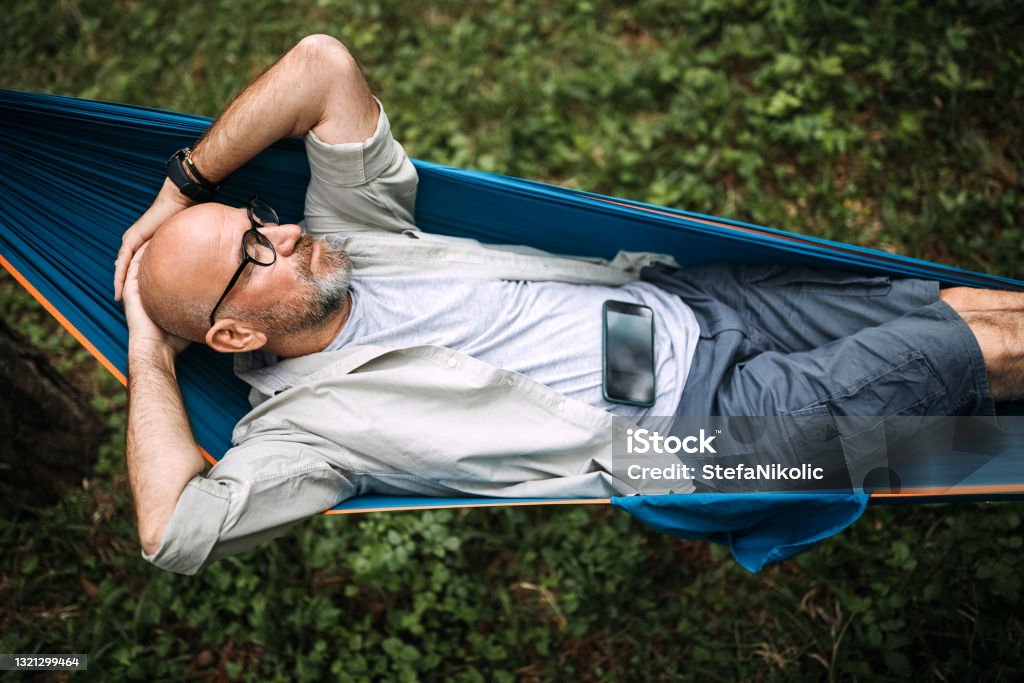 This is my life Senior man laying on hammock in nature and using smart phone Relaxation Stock Photo