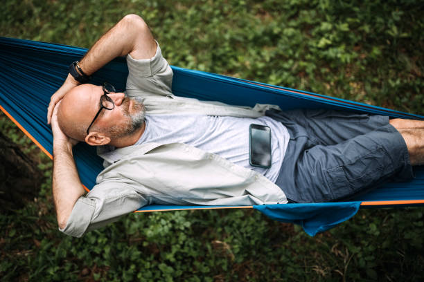 This is my life Senior man laying on hammock in nature and using smart phone hammock stock pictures, royalty-free photos & images