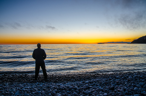 Man standing at beach of stone of Lake Superior during sunset of springtime