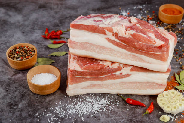 Two pieces of raw pork belly with garlic isolated on gray background. Two pieces of raw pork belly with garlic and bay leaves on gray background. uncooked bacon stock pictures, royalty-free photos & images