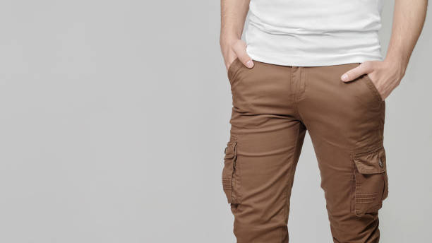 Man wearing cargo pants with hands in pockets on grey background.