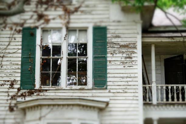Window and shutters in run down older home with peeling paint. Selective focus.